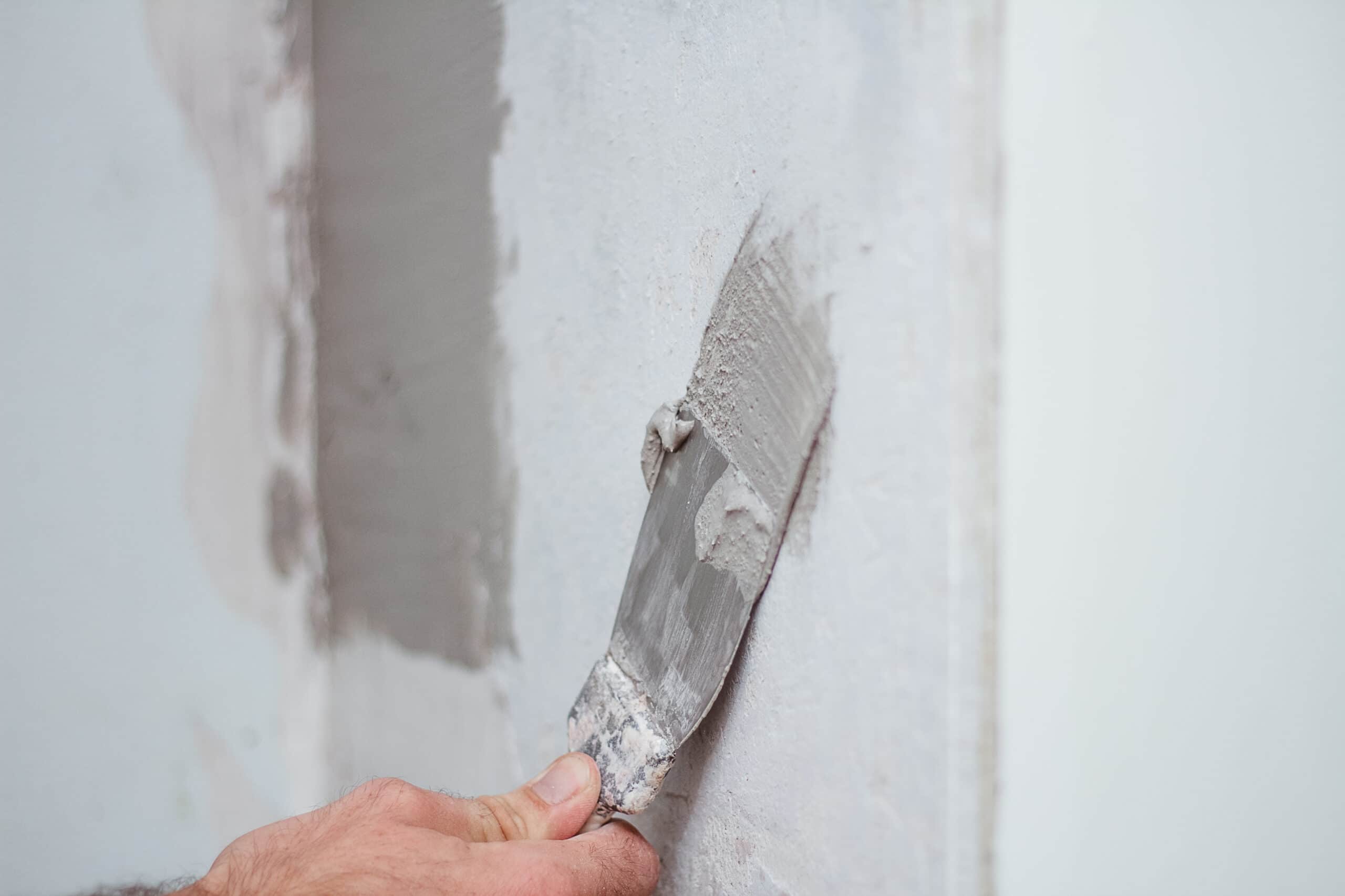 A man's hand using a trowel to apply skim coating to a wall for waterproofing purposes.