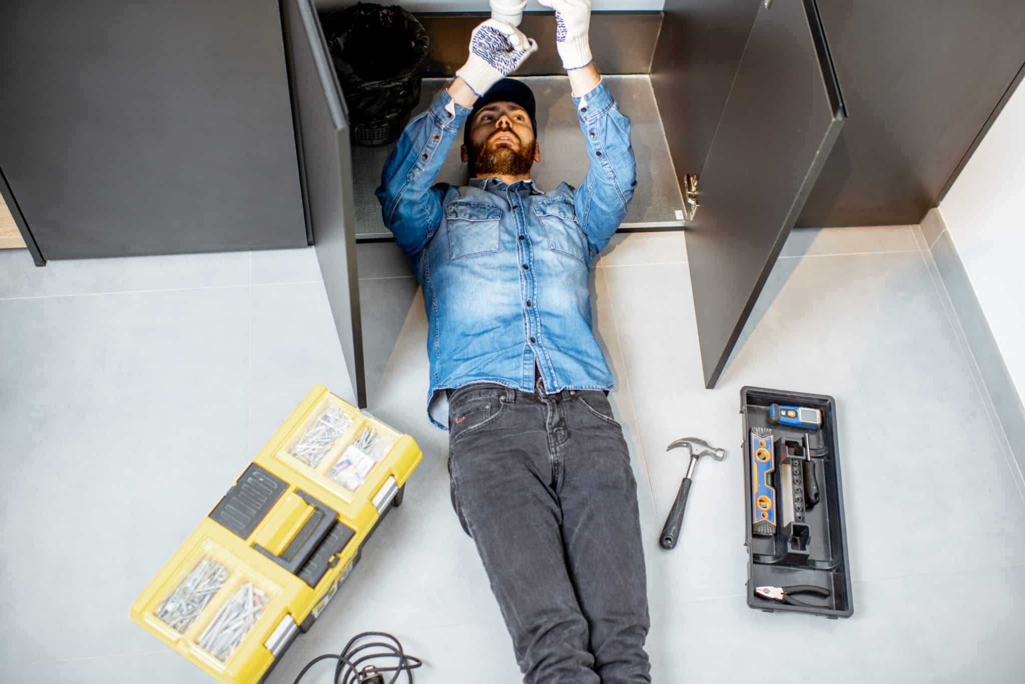 A man performing home plumbing repair while lying under the kitchen sink on the floor