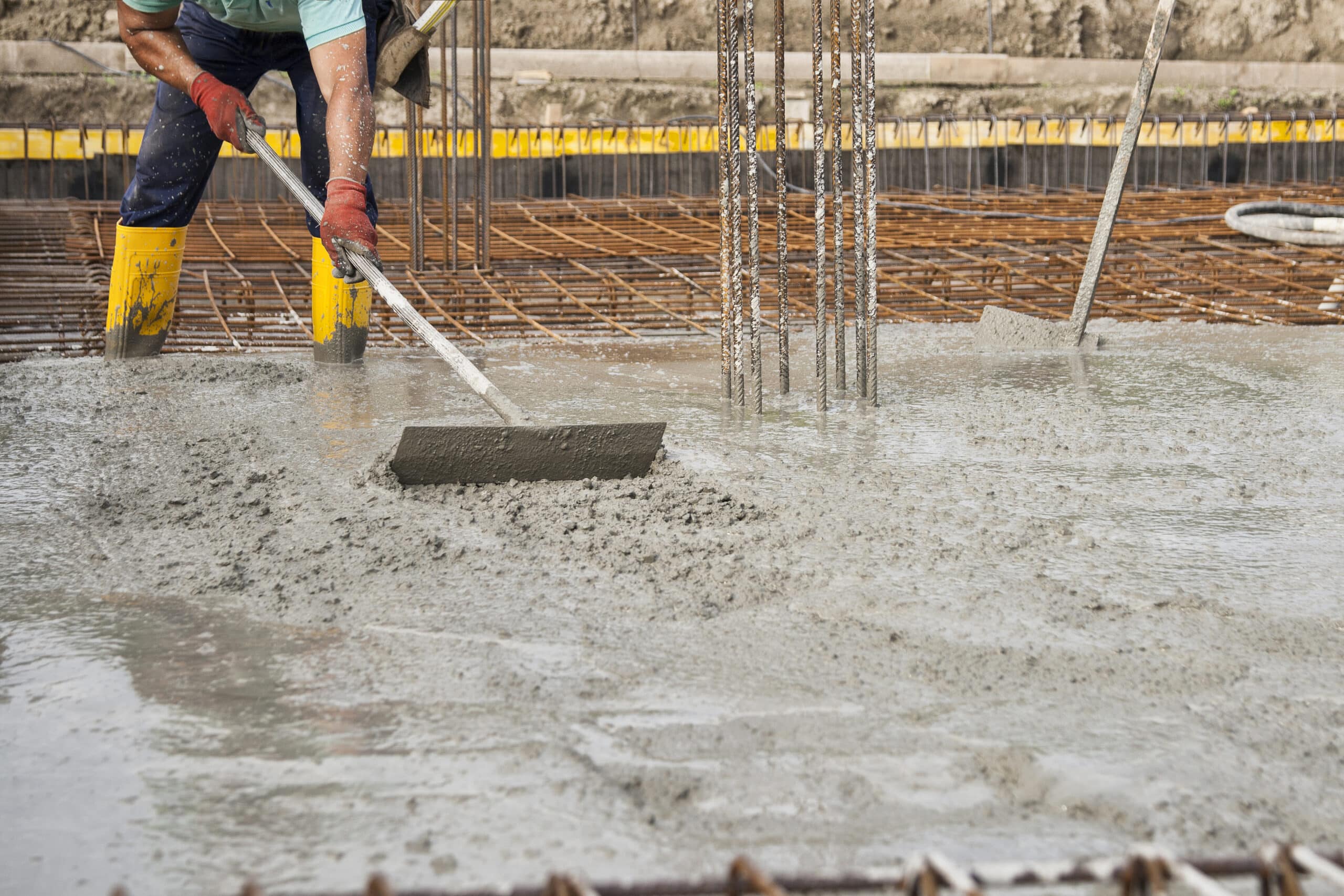 A construction worker smoothing foundation cement at building site, highlighting importance of proper foundation for construction.