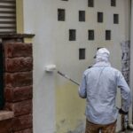 Painter worker adding undercoat foundation paint onto wall with roller at residential building in